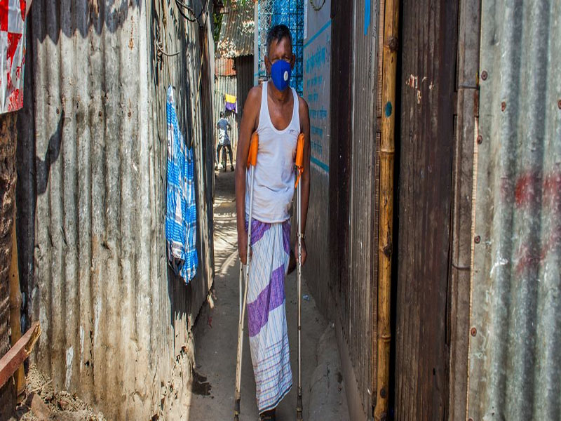 © PNUD Bangladesh/Fahad Kaizer. Un hombre con discapacidad camina usando muletas en un barrio de Bangladesh